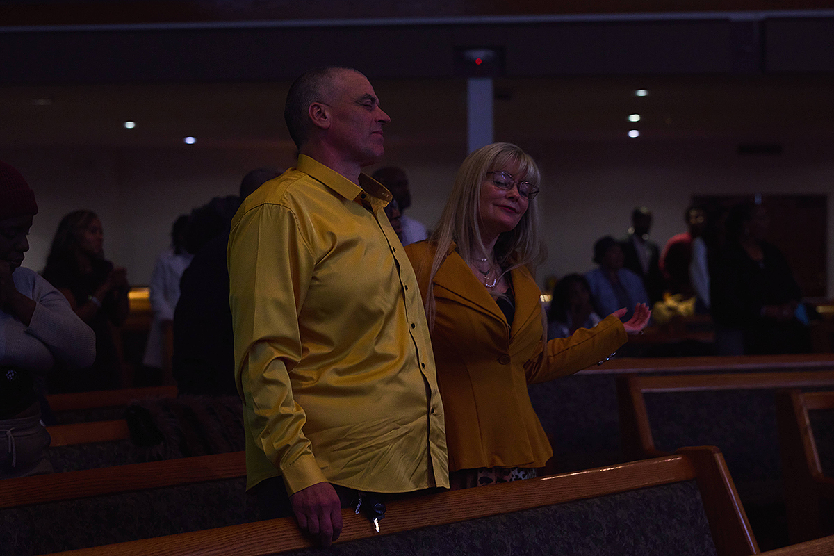 Couple standing together in worship, eyes closed and hands lifted in reverence.