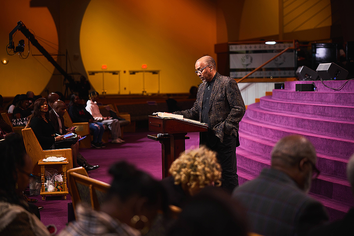 Bishop David G. Evans preaching from the pulpit during a worship service, with an attentive congregation in the background